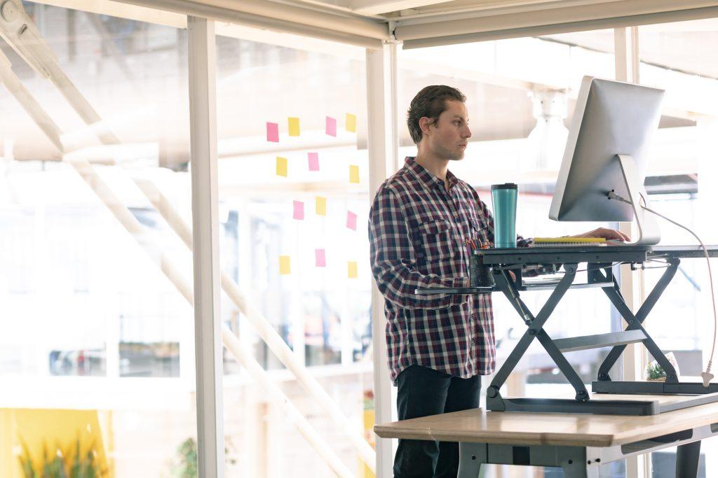 Side view of a person working on computer at standing desk in office